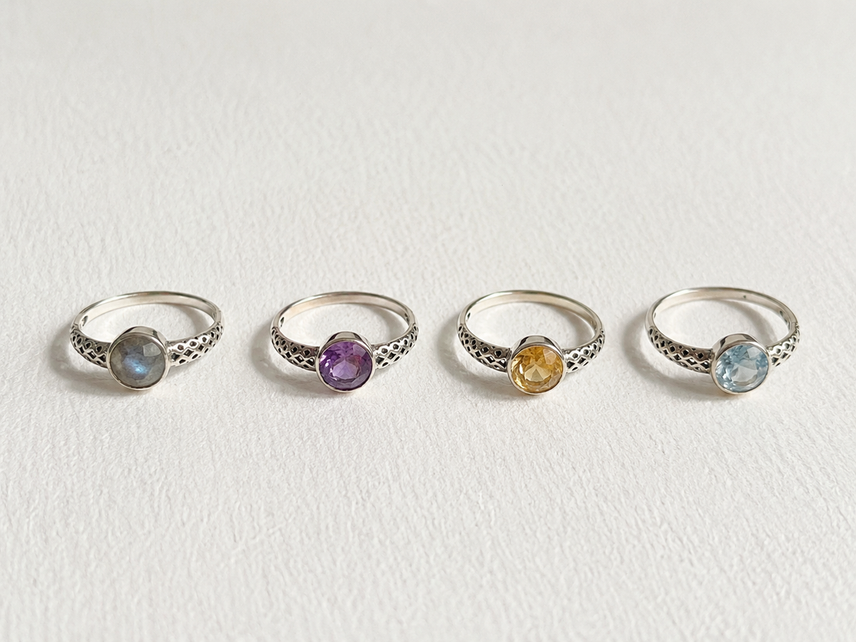 Four silver rings with gemstones are arranged in a row on a white background.