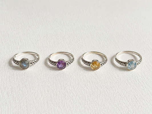 Four silver rings with gemstones are arranged in a row on a white background.