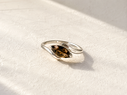 A silver ring with a large, dark brown gemstone is displayed on a white surface.