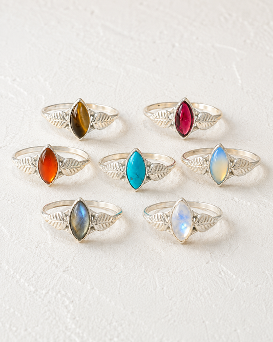 a collection of seven silver rings, each adorned with a unique gemstone. The rings are arranged in a circular pattern, showcasing the variety of gemstones and designs.