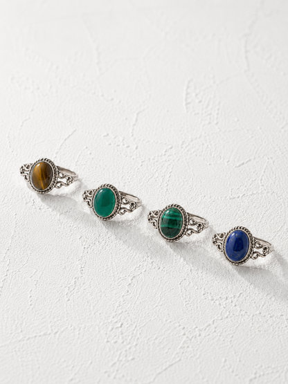 Four silver rings with colorful gemstones are arranged in a row on a white background.