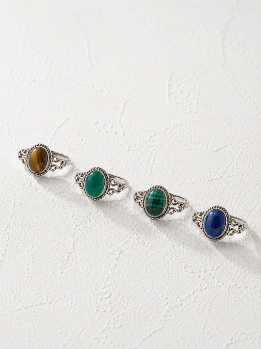 Four silver rings with colorful gemstones are arranged in a row on a white background.