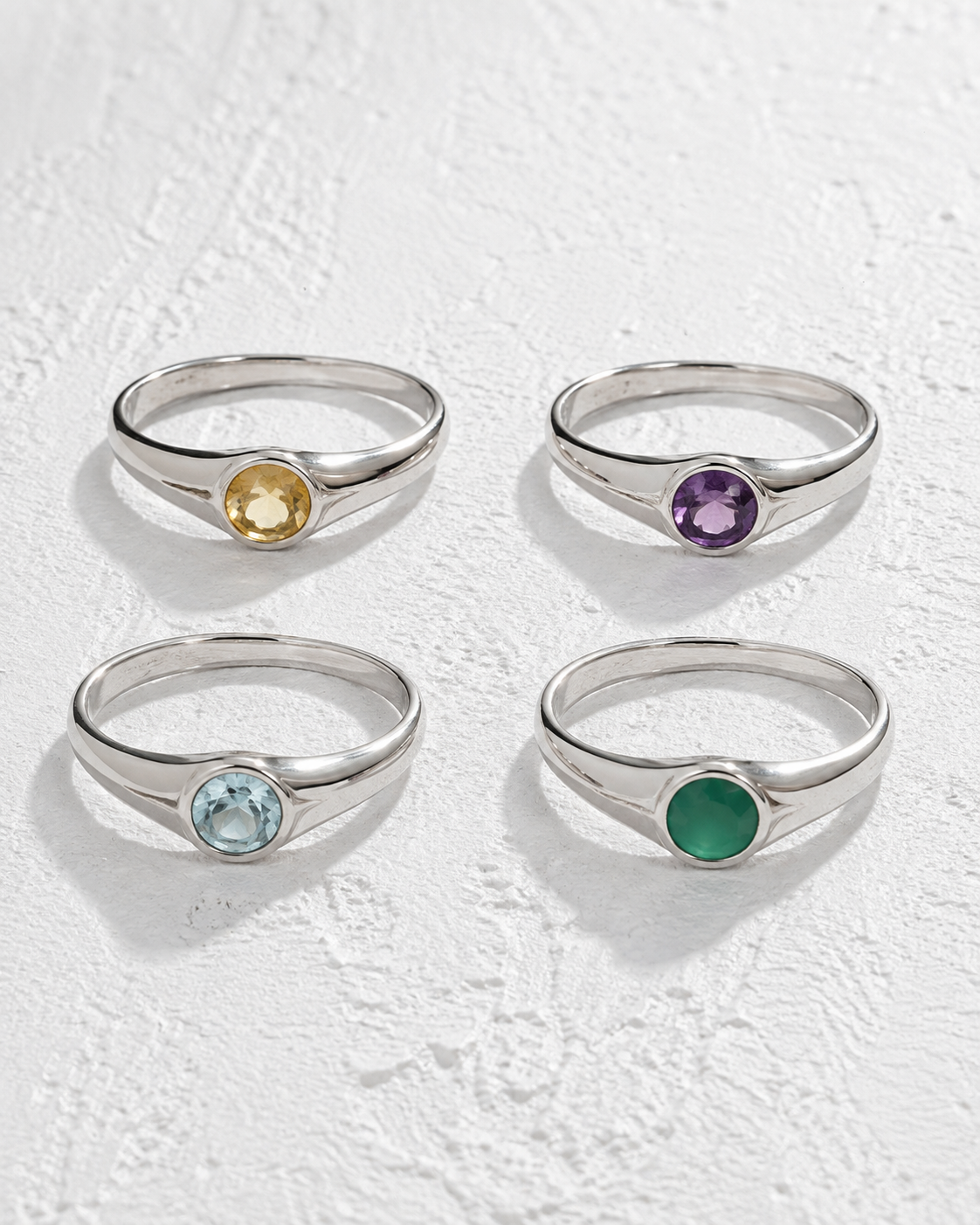 four silver rings with gemstones, each with a different colored gemstone.