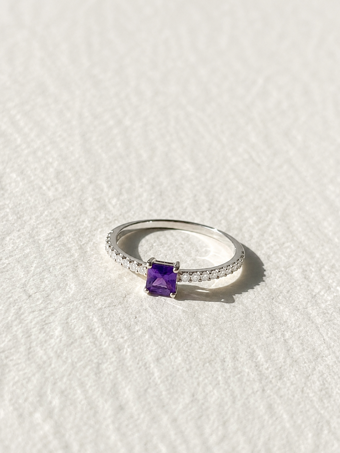 A silver ring with a purple gemstone, likely a diamond, set in the center of the band.