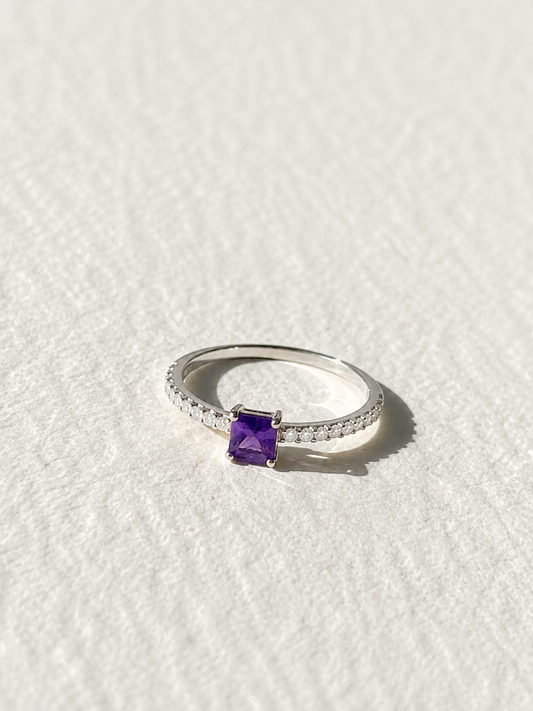 A silver ring with a purple gemstone, likely a diamond, set in the center of the band.