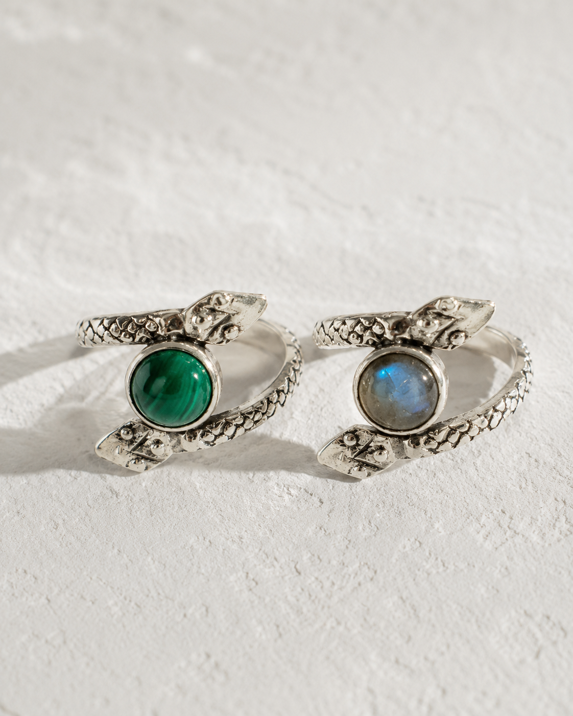 Two silver rings with snake-like designs and gemstones are displayed on a white surface.