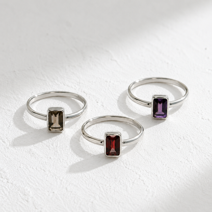 Three silver rings with gemstones are displayed on a white surface.