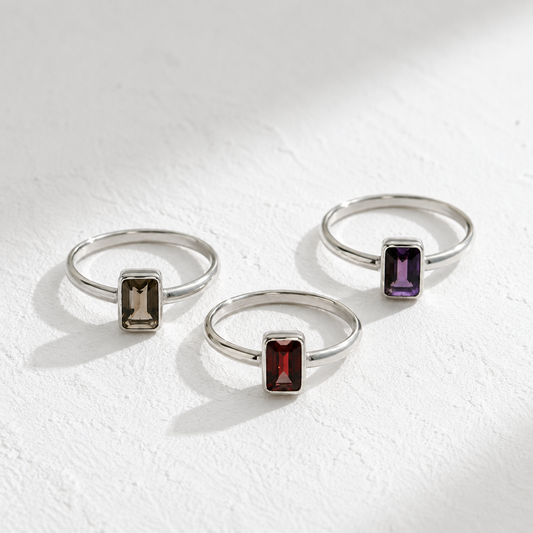 Three silver rings with gemstones are displayed on a white surface.
